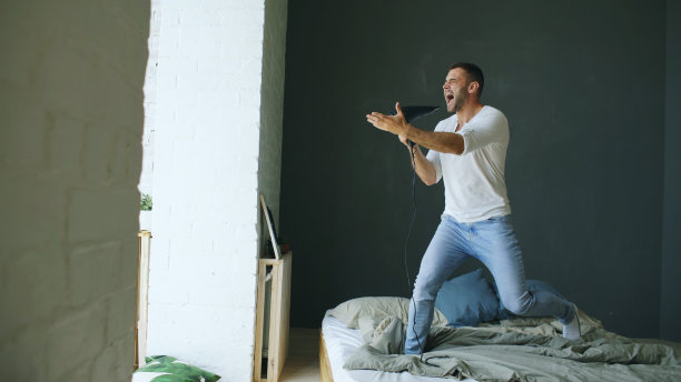 年轻人对着吹风机唱歌，在卧室的床上跳舞图片下载