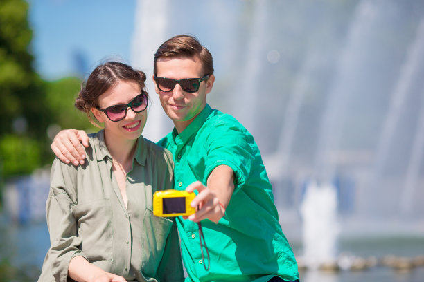 一对情侣在喷泉边自拍。年轻男子在街上拍女人的照片，在夏天笑着玩。图片下载