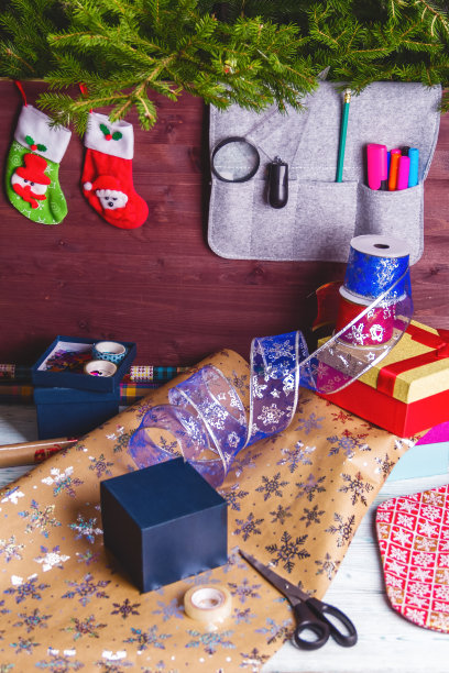 包装圣诞礼盒。新年圣诞包装纸，丝带，蝴蝶结线，剪刀，圣诞树在木制的背景上。冬季新年图片下载