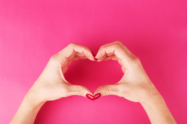 女人的手在粉红色的背景上形成一个心形的象征图片下载