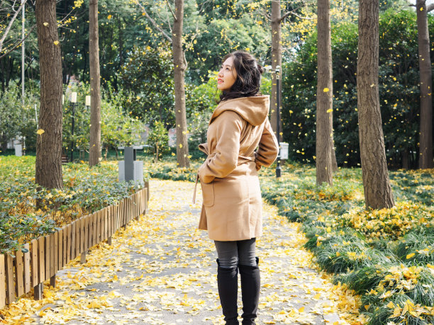 一个美丽的中国女孩站在秋天公园的落叶中。图片下载