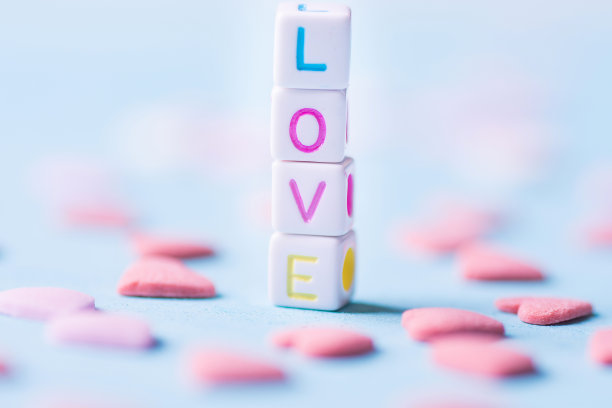 由堆叠的字母立方体构成的单词爱。粉红色的糖粒散布在浅蓝色的背景上。浪漫情人节慈善概念。贺卡海报横幅模板图片下载