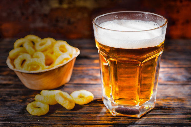 深色木桌上放着小点心，盘子旁边放着大玻璃杯，新鲜的淡啤酒图片下载