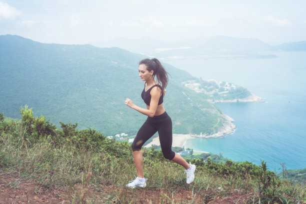健身女运动员穿着黑色运动服做有氧运动，跑步在山与鼓舞人心的海景图片下载