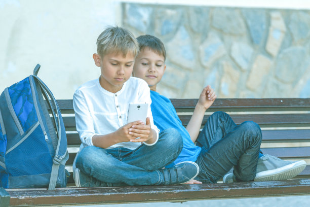 男孩们拿着手机坐在户外的长椅上图片下载