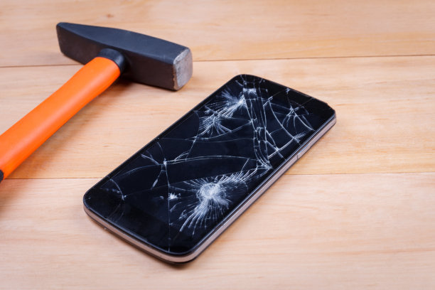 一个锤子在一个屏幕破碎的智能手机旁边。在木制的背景上。特写镜头。图片下载