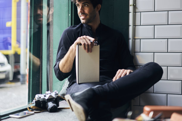 开朗有吸引力的熟练男子看窗外，看路人为未来的图片展示有趣的肖像坐在室内，享受美好的一天图片下载