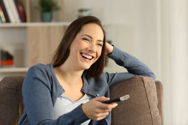 坐在家里沙发上笑着看电视的女孩图片下载