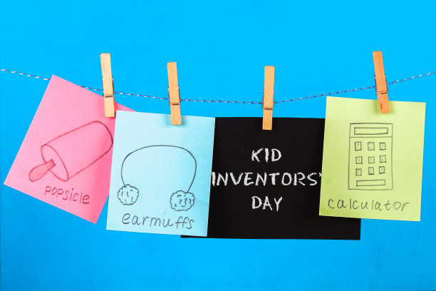 小纸条挂在衣钉上，上面画着孩子们的发明——popsikl, Earmuffs, calculator在蓝色的背景上。短信-孩子发明家日。图片下载