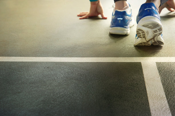 手与蓝色运动鞋女子跑在起跑线在体育馆地板的背景图片下载