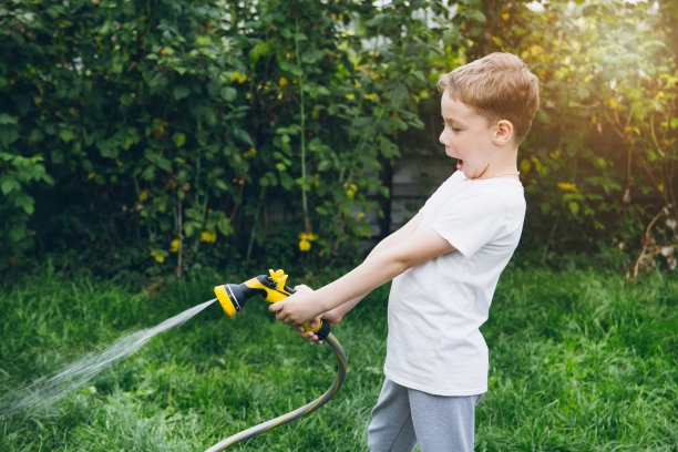 小男孩用水管浇花园。图片下载