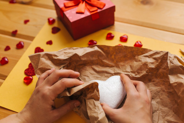 女孩拿着一个心形的符号，用牛皮纸包好，准备送给别人。附近有各种象征这一事件的物品。图片下载