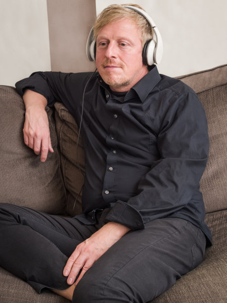 一个戴着白色耳机坐在沙发上的成熟男人。图片下载