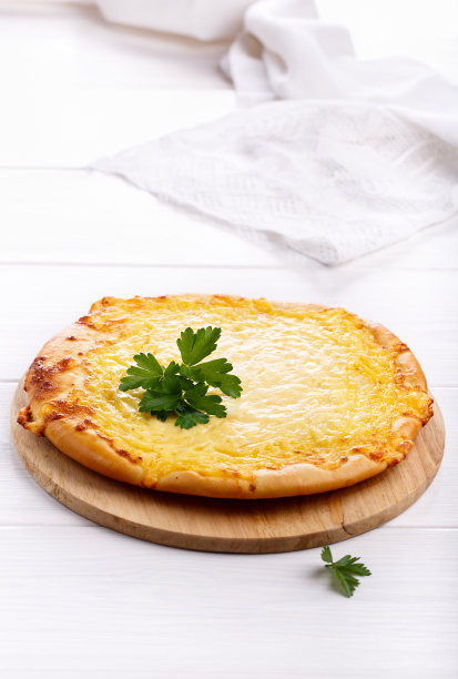 加奶酪的扁平面包。白色的桌子上放着一整块大饼披萨。图片下载