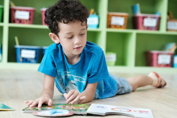 美国男孩在幼儿园教室里躺着看书，孩子的教育理念图片下载