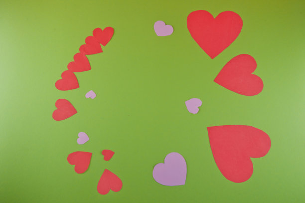 不同大小的剪纸红色，粉红色的心放在绿色的背景上图片下载