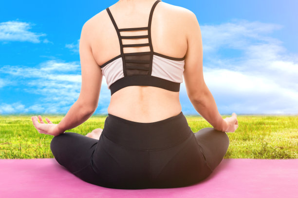 在蓝天背景下的绿草上练习瑜伽的女人图片下载