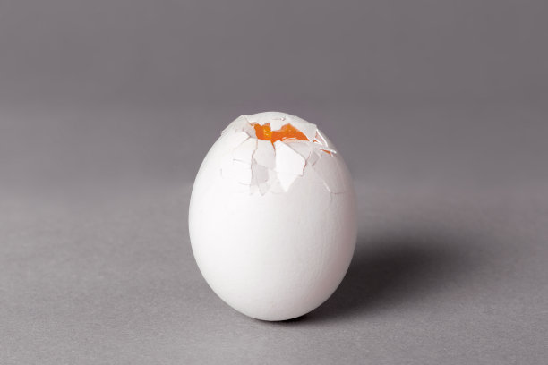破的白色鸡蛋，有裂缝，可以看到蛋黄。灰色背景图片下载