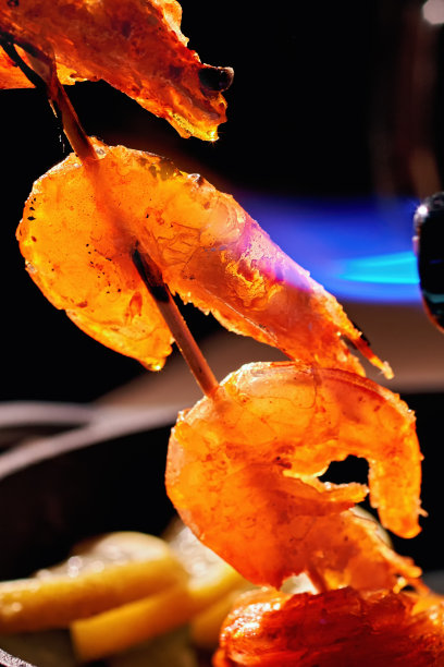 虾仁用木串用燃气火把烧。用专业的厨师长设备在背景煎锅上配上装饰，烹制美味新鲜的海鲜。垂直的照片。图片下载