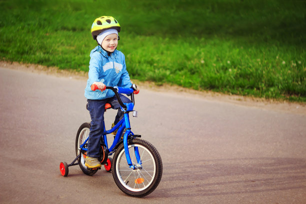 男孩在公园的城市小路上骑自行车。小自行车手在头盔骑自行车。图片下载