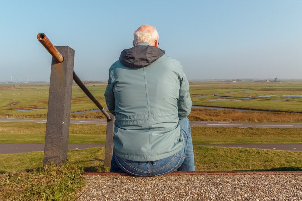 一位年长的男同学坐在荷兰北部坎珀杜因附近的堤坝上，俯瞰着周围的风景图片下载