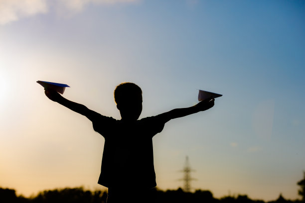 快乐的孩子在夕阳下玩纸飞机。孩子们在户外上课。生活方式图片下载