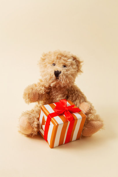棕色的玩具熊，浅米色背景上有一个礼物。作为贺卡的概念，适用于情人节、母亲节、生日图片下载