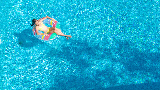 鸟瞰图的女孩在游泳池从上面，孩子游泳在充气圈甜甜圈和有乐趣的水在家庭度假图片下载