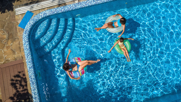 从上面鸟瞰游泳池里的一家人，快乐的妈妈和孩子们在充气甜甜圈上游泳，在水上玩得很开心图片下载