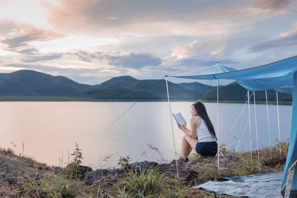 年轻的亚洲女性旅游放松的假期。在山上露营，在湖边看书图片下载