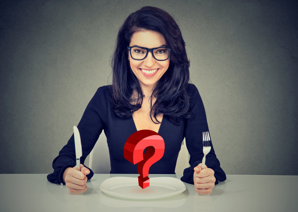 快乐的女人戴着眼镜拿着刀叉坐在空盘子的桌子旁图片下载