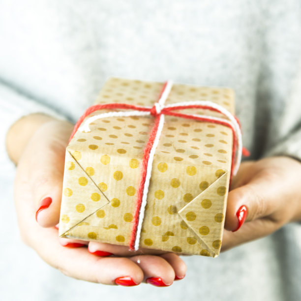 圣诞礼物包在牛皮纸波尔卡点在女性的手与红色美甲图片下载