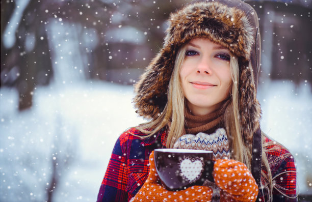 情人节，女人拿着冬天的杯子，用心靠近白雪皑皑的背景。图片下载