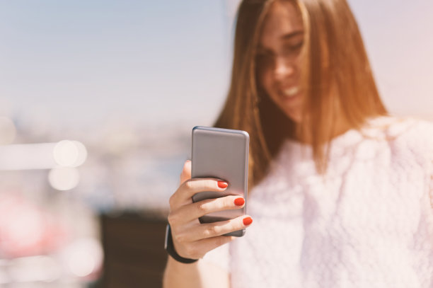 女孩拿着手机的手放在夕阳的背景上，柔焦，城市的场景图片下载