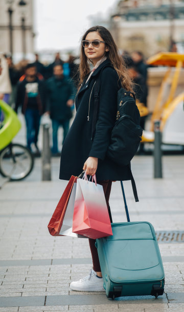 年轻的女游客提着旅行箱和购物袋走在巴黎图片下载