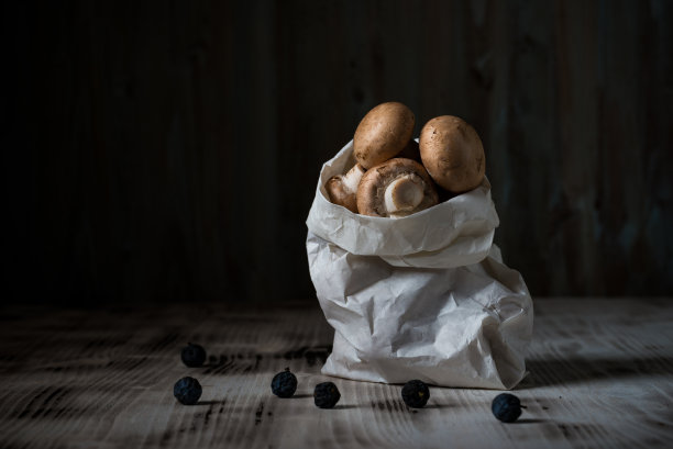 与几只棕色食用蘑菇的横向照片。生的香槟装在白色的纸袋里。包是在古老的木板与洒黑刺。下一个背景是木板。图片下载
