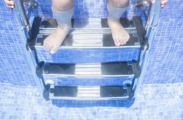 一个女孩坐在游泳池的梯子上，腿在水下图片下载