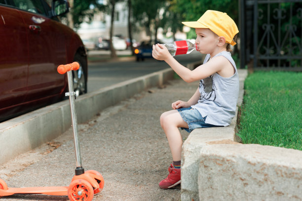 5岁的男孩，在公园的路上骑着滑板车。孩子喝水。家庭度假图片下载