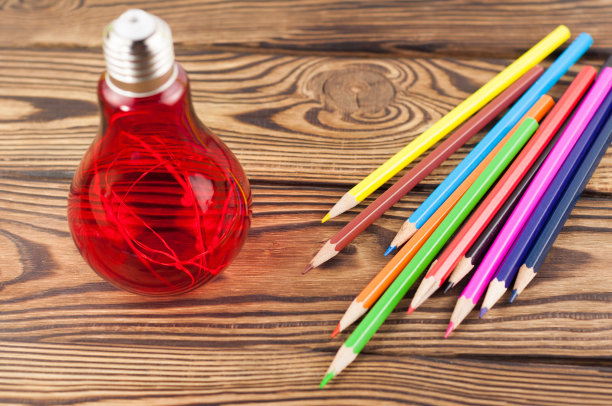 彩色的木制铅笔旁边的电灯泡在旧木制的乡村棕色的桌子上图片下载