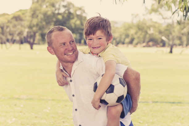 年轻快乐的父亲背着他兴奋的7或8岁的儿子一起踢足球在城市公园的花园摆出甜蜜和爱拿着球在爸爸和男孩的关系图片下载