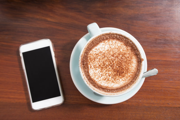 木桌上放着一杯热巧克力和一部智能手机。图片下载