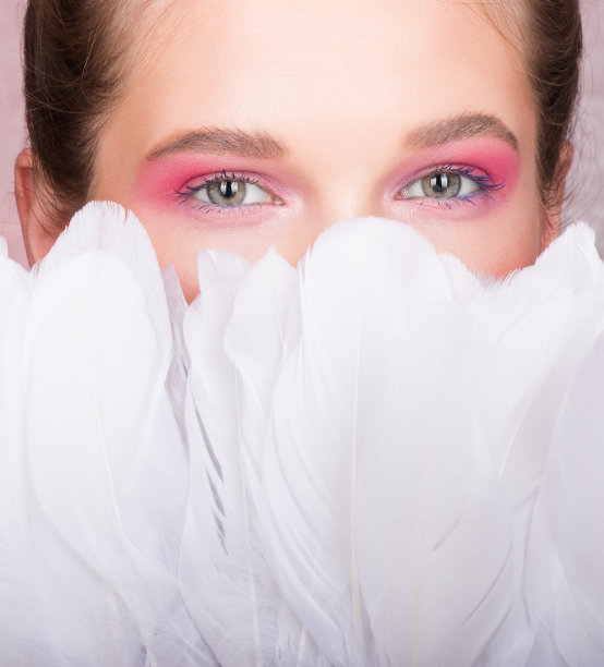 美丽的肖像。年轻美丽的女子的脸与白色的羽毛合拢图片下载