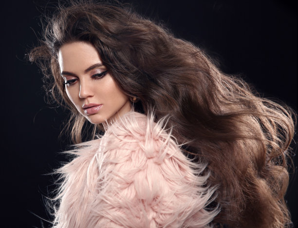 穿着粉红色裘皮大衣的时髦黑发女人。性感迷人的女孩与长健康的发型和闪光的晚妆，摆出孤立的黑色工作室背景。卷发的女士。图片下载
