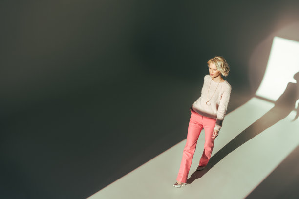 高角度的美丽的年轻女子在时尚的粉红色衣服走在工作室图片下载