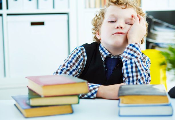 疲惫不堪的小男孩正坐在一张堆满书的桌子旁图片下载