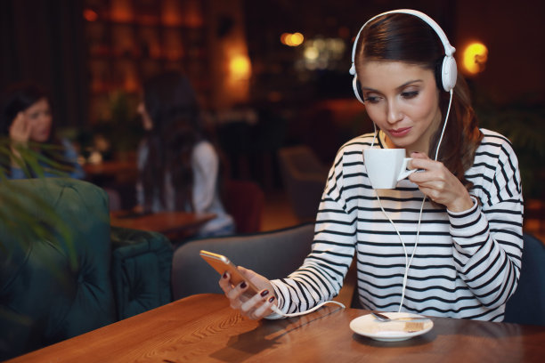年轻女子戴着耳机听音乐，在咖啡馆喝咖啡图片下载