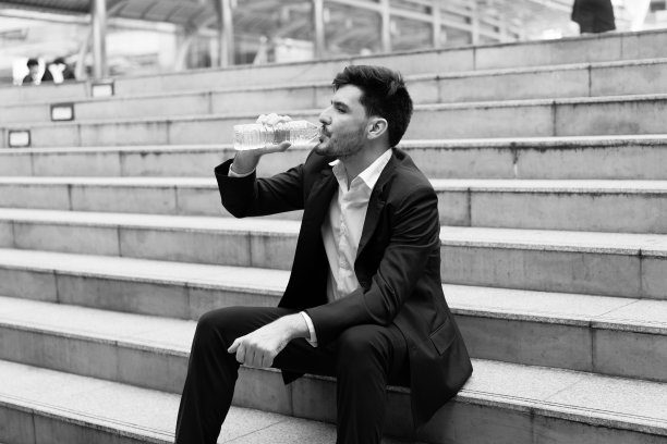 图片处理:快乐商人在户外楼梯上从瓶子里喝水，黑白色调。图片下载