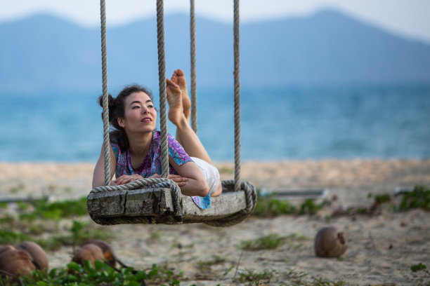 年轻的混血女子躺在沙滩上的木制秋千上。图片下载