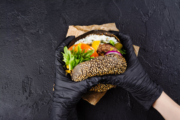 女人的手在黑色橡胶手套拿着多汁的黑色面包汉堡图片下载