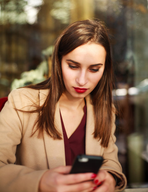 穿着大衣的好女孩在夏天的咖啡馆里用手机图片下载